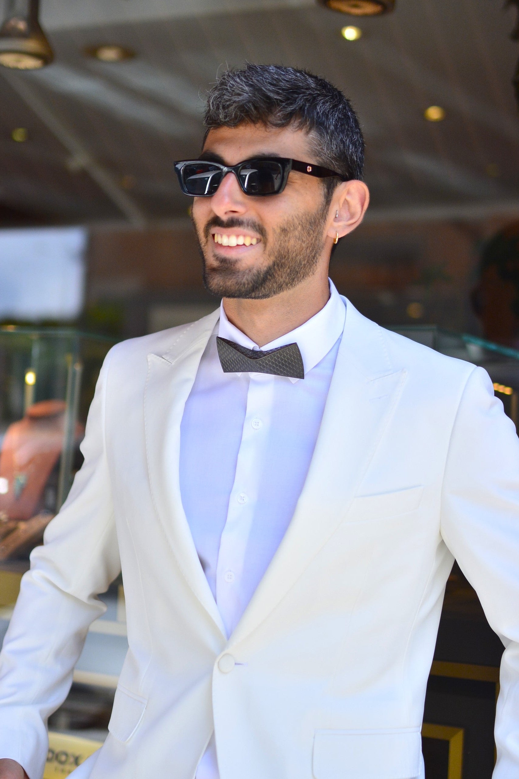 Man wearing a white suit and black bow tie by unities in an indoor setting