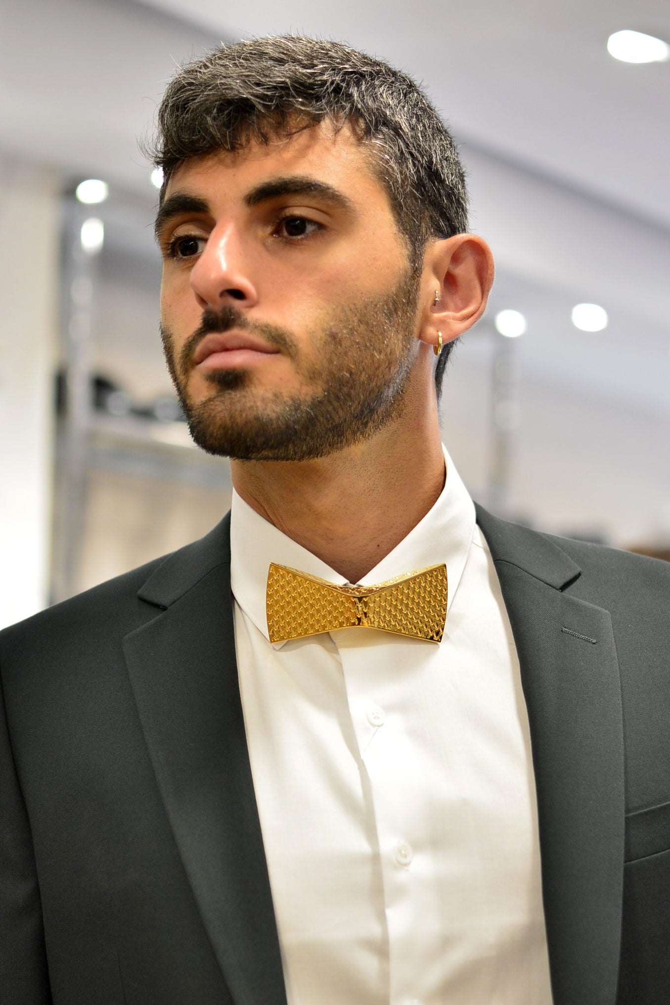 Man wearing a black suit with a white shirt and gold bow tie indoors.