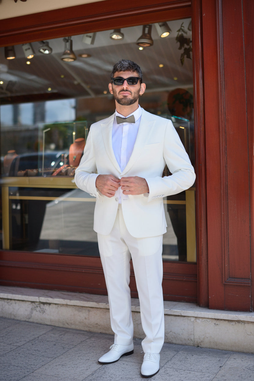 Man in a white suit and black bow tie by unities  standing in front of a store entrance