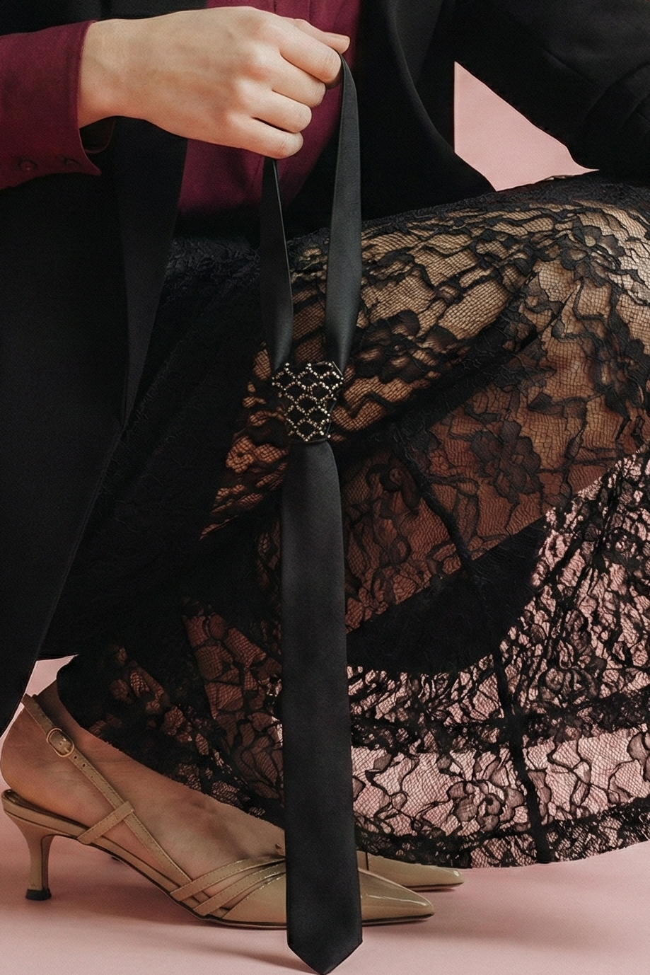 Person wearing a black coat, red shirt, and lace skirt with a pink background