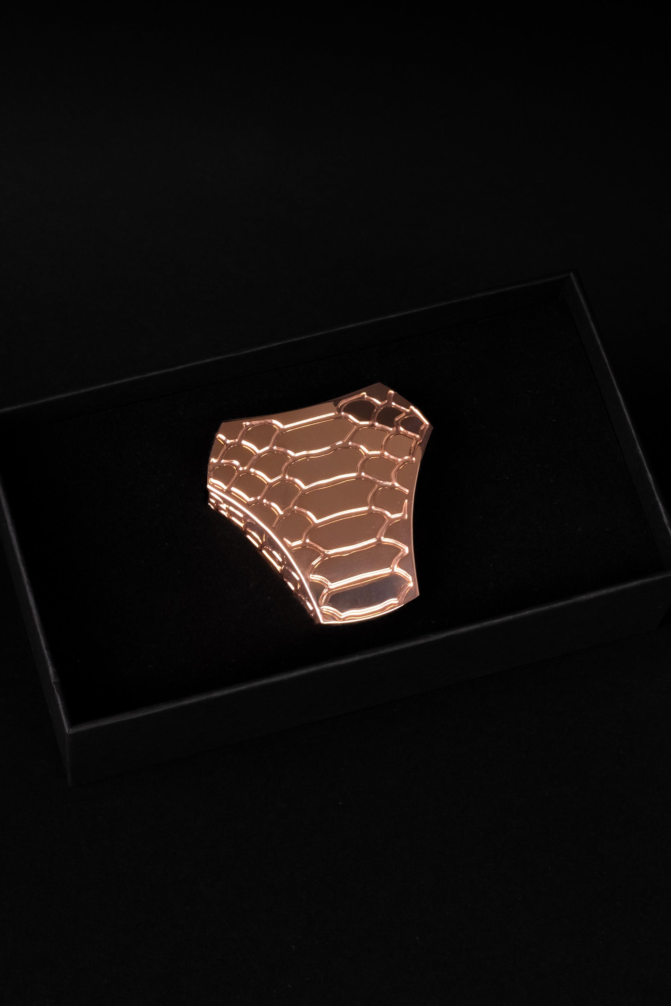 A metallic rose gold textured ring displayed inside a black presentation box against a solid black background.